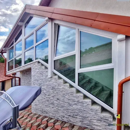 Verandă închisă cu geamuri termopan, structură albă și finisaj exterior din piatră decorativă