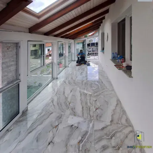 Interior de verandă închisă cu pereți din termopan, acoperiș cu grinzi de lemn și pardoseală lucioasă