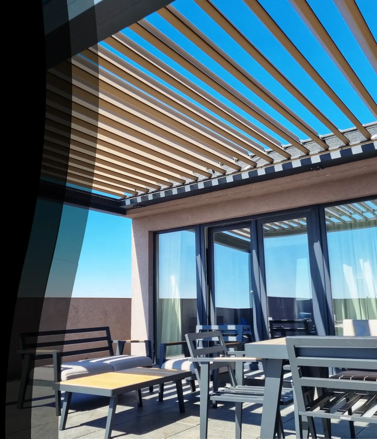 Pergolă bioclimatică modernă instalată pe o terasă elegantă, cu mobilier de exterior din aluminiu și acoperiș reglabil din lamele. 