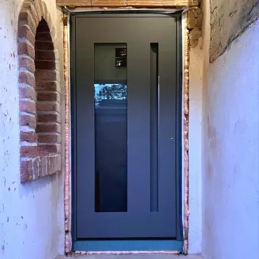 Ușă metalică antracit cu sticlă decorativă, instalată într-o nișă îngustă în locul unei uși vechi.