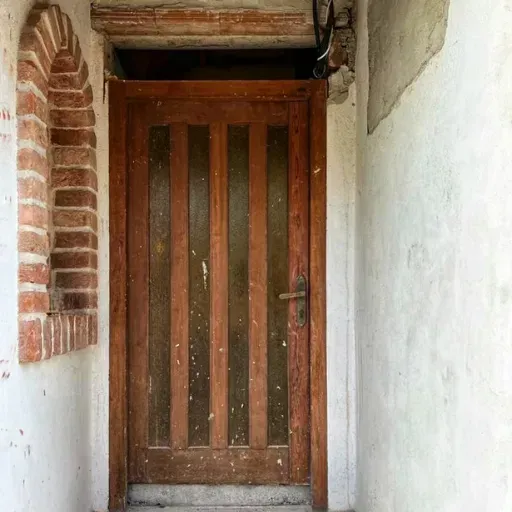 Ușă veche din lemn, montată într-o nișă rustică cu elemente de cărămidă decorativă.
