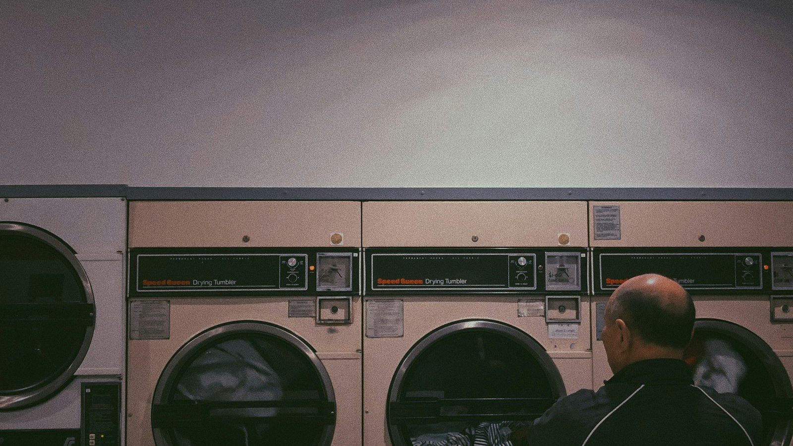 Man loading clothes into a front-load dryer at a laundromat