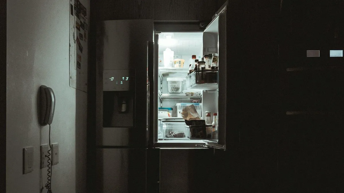 Open stainless steel French door refrigerator glowing in a dark kitchen