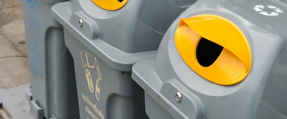 A close-up view of two grey outdoor recycling bins with bright yellow, crescent-shaped disposal openings.
