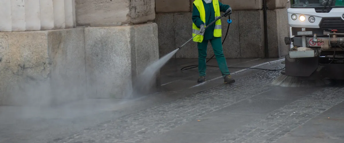 A close-up of a yellow pressure washer nozzle cleaning a speckled concrete surface with a stream of water.