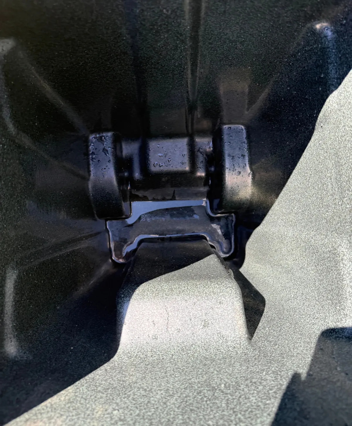 Close-up of water pooling in a dark, textured plastic container around a wet hinge mechanism.