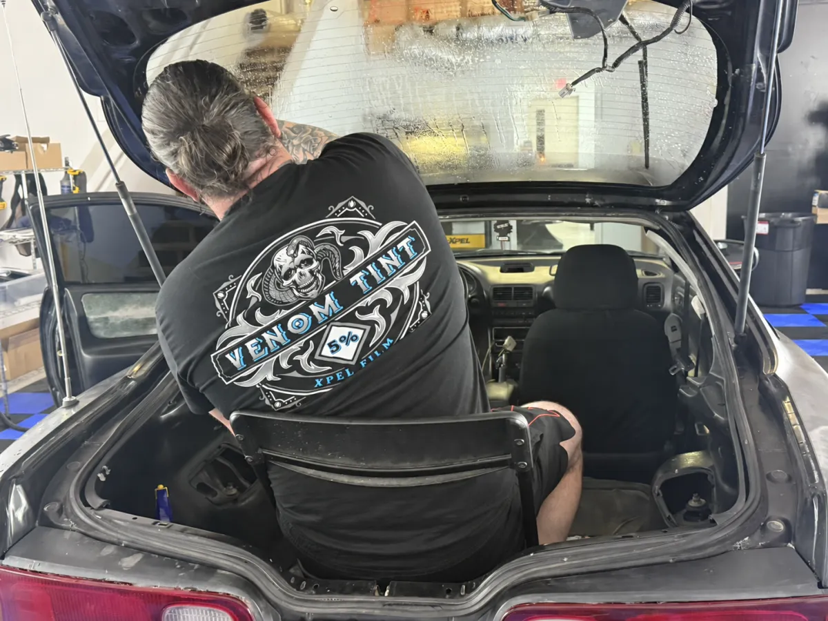 Venom Tint installer working on a vehicle’s rear glass inside the shop