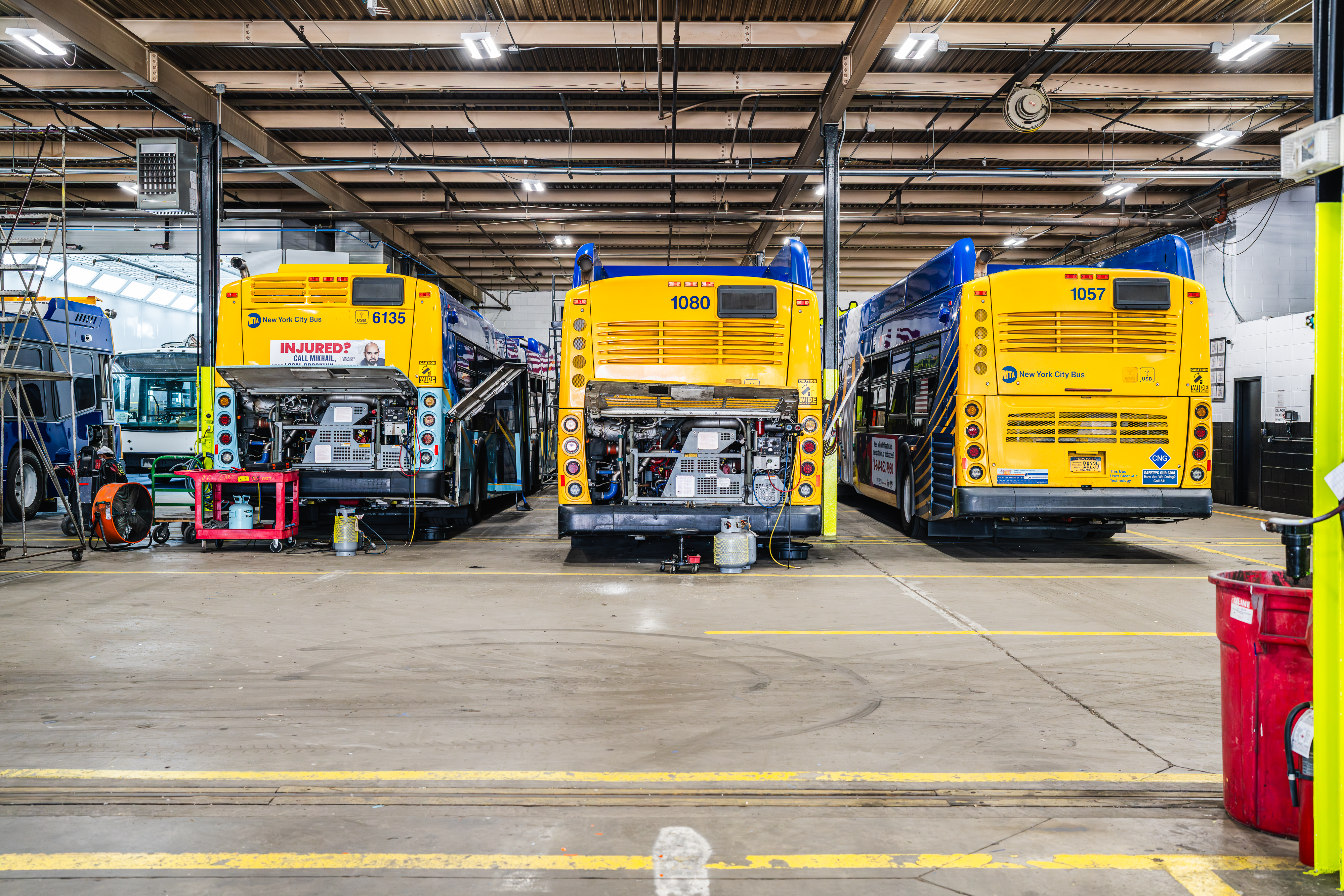 Row of transit buses undergoing preventive maintenance inside NEBR facility