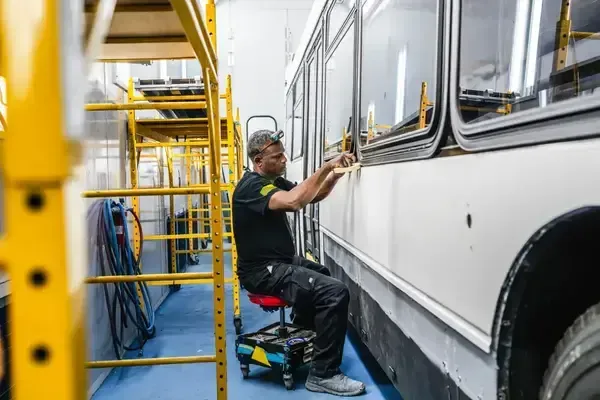 Automotive painter preparing and refinishing exterior surfaces on a transit bus