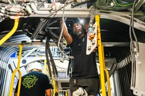 Electrical technicians working on wiring and high-voltage systems inside a hybrid bus