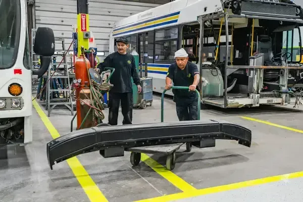 NEBR technicians moving transit bus bumper inside maintenance shop