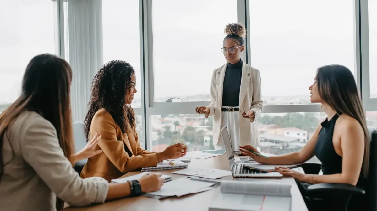 Human-Centered Leadership: 7 Mantras for Creating Safe Teams — A professional meeting in a modern office where a leader in a light suit actively engages with three attentive team members seated at a conference table, symbolizing trust, collaboration, and psychological safety.