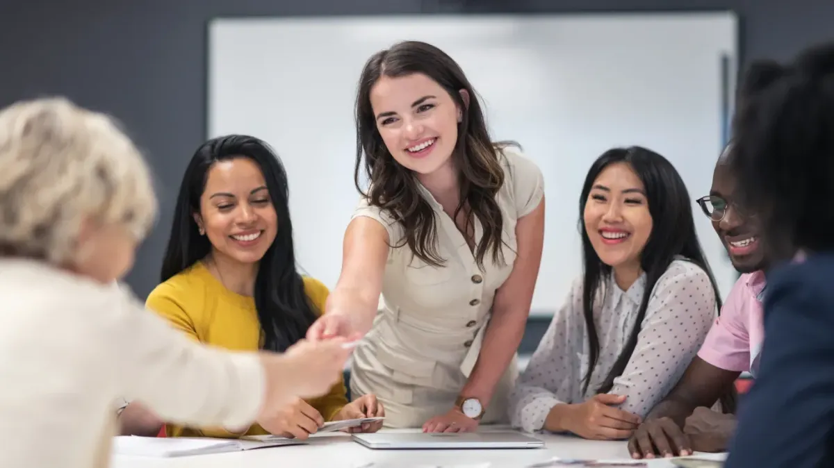 Mindful Communication: 7 Mantras for Effective Leadership — A collaborative group meeting where five people sit around a table, smiling and engaged, as one participant stands to shake hands, symbolizing trust, respect, and effective leadership through mindful communication.