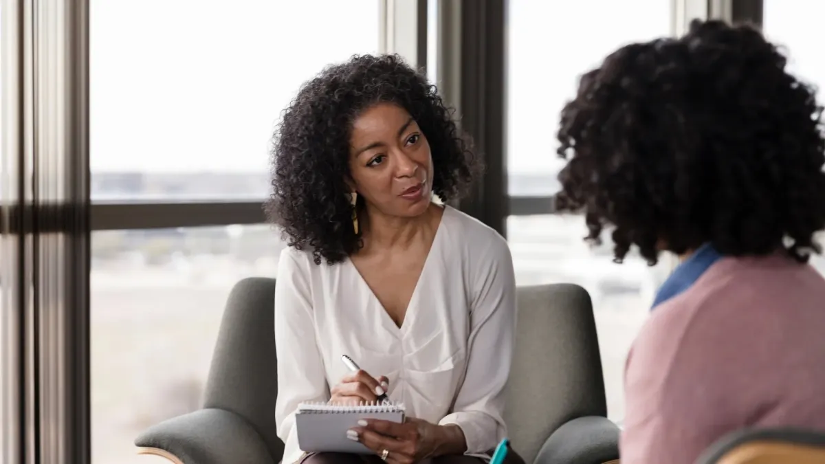 A therapist taking notes while listening attentively to a client during a counseling session, representing mental health habits that last beyond Awareness Month through ongoing support, open conversation, and consistent self-reflection.
