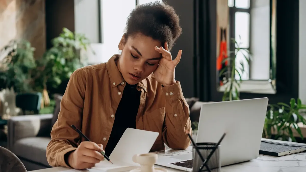 Professional woman working at a desk with a laptop and notebook, practicing focus and self-awareness through Mindful Performance Mantras for High Achievement, balancing productivity, resilience, and mental wellbeing.