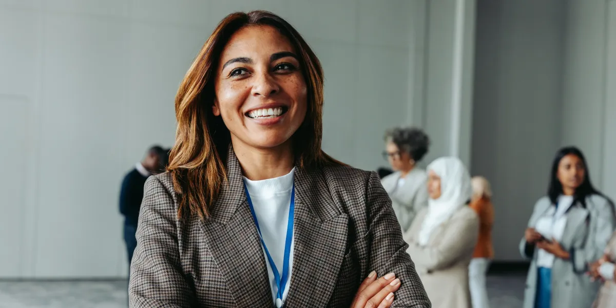 A confident professional woman stands in an office with colleagues in the background, representing Authentic Leadership Mantras for Leading with Integrity through confidence, authenticity, and purposeful leadership.