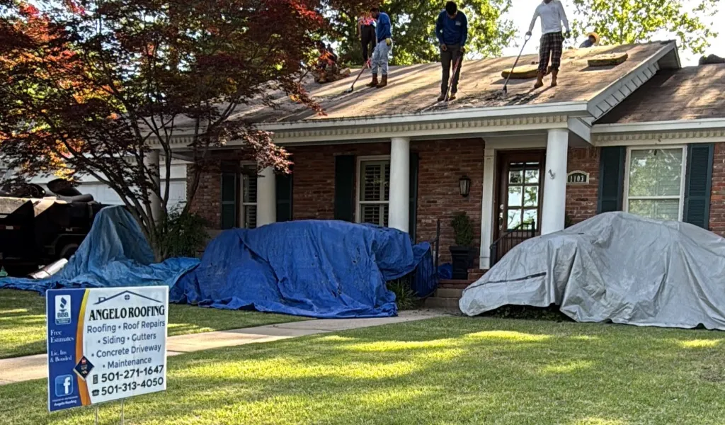 A group of three men working on a roof while the Angelo Roofing sign can be seen below on the ground.