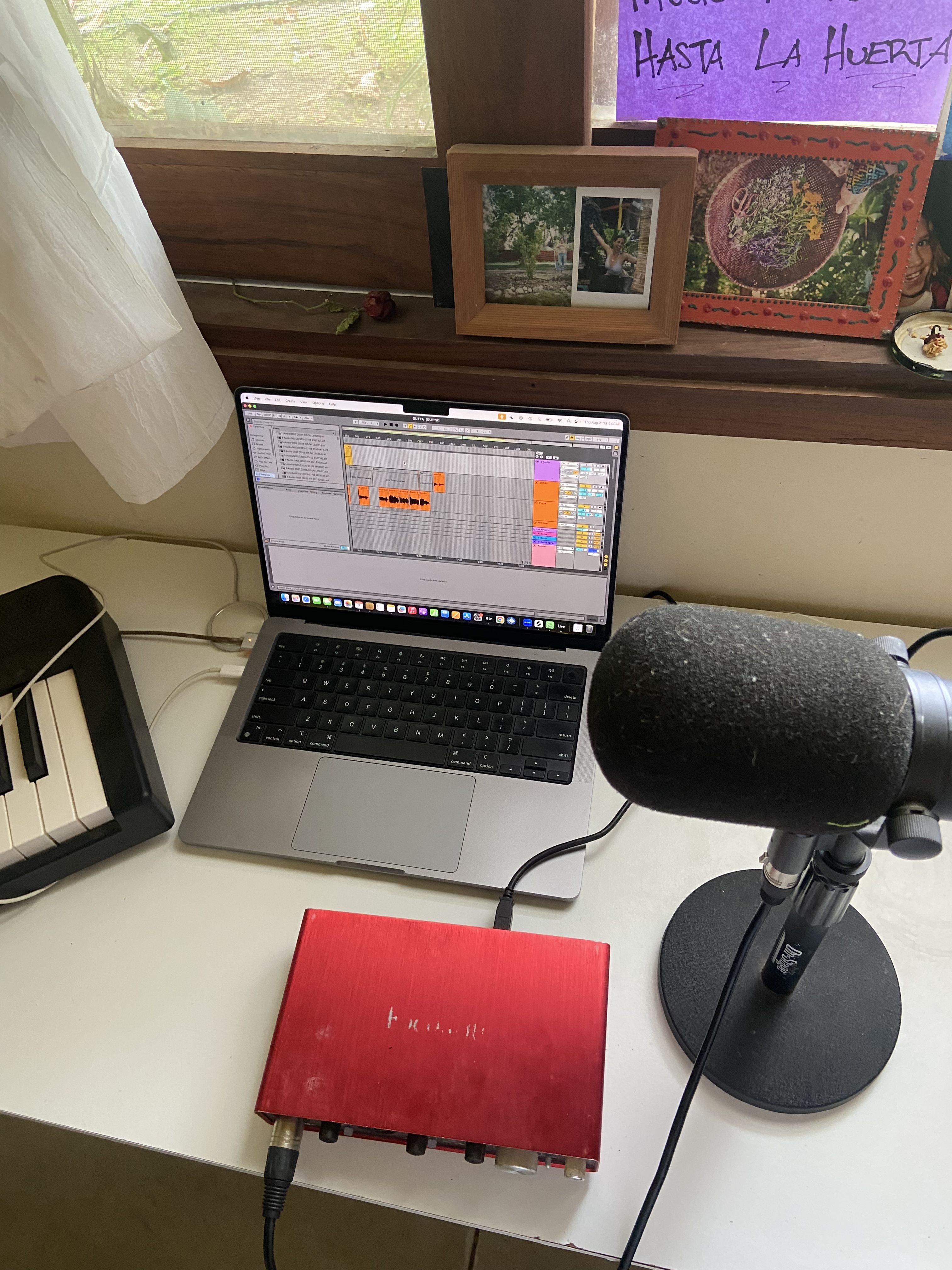 A close-up of a hand marking a calendar with a pink pen, a guitar resting nearby, and a soft-focus background of sheet music and pastel flowers, evoking daily progress and gentle motivation.