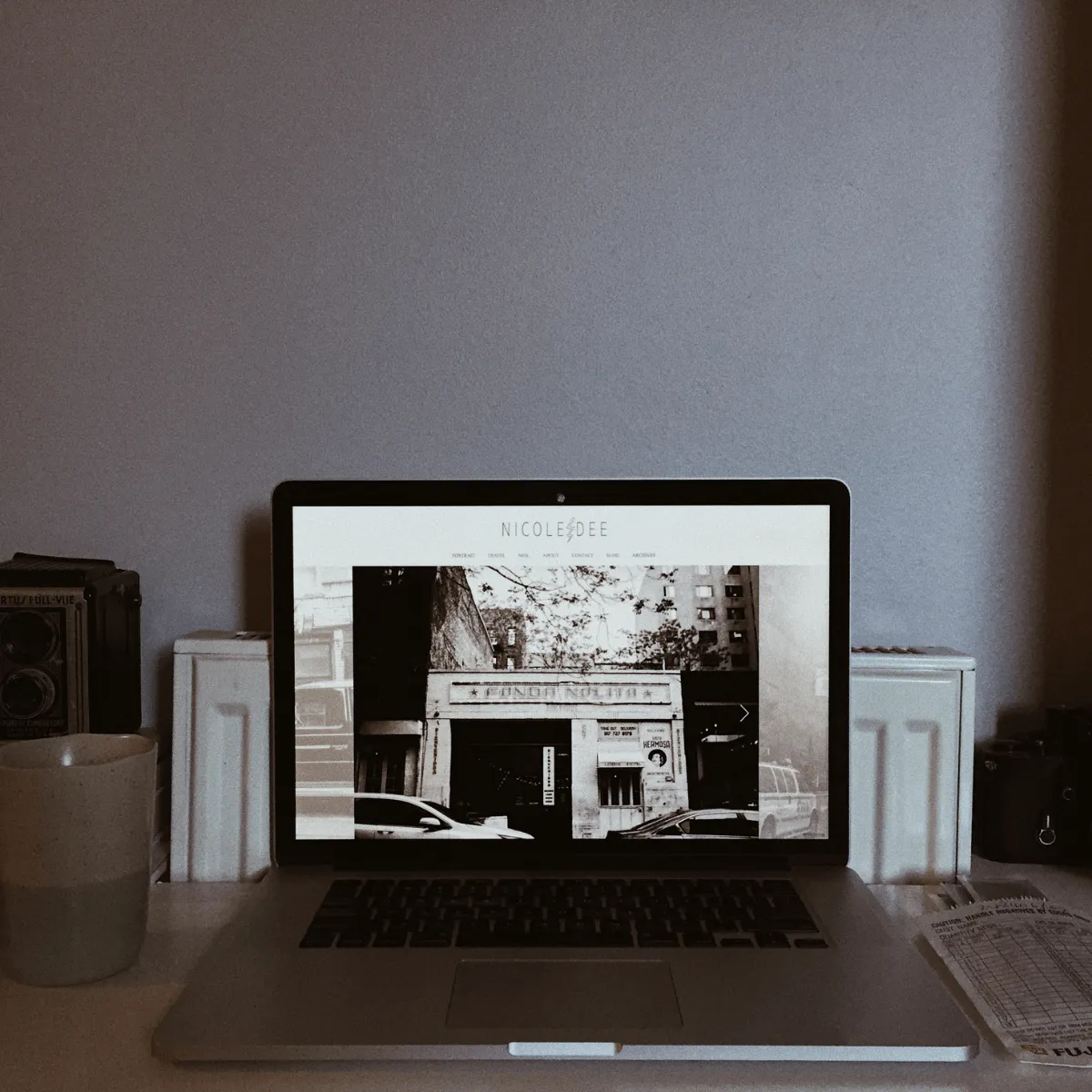 Laptop vor grauer Wand. Auf dem Bildschirm ist ein schwarz/weißes Bild mit einem Gebäude zu sehen.