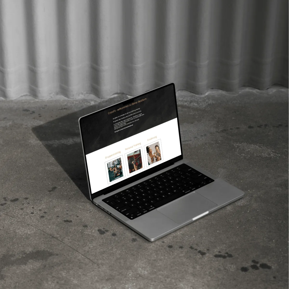 Laptop auf grauem Steinboden vor grauer, geriffelter Wand. Ein Bild einer Website ist auf dem Bildschirm zu sehen.