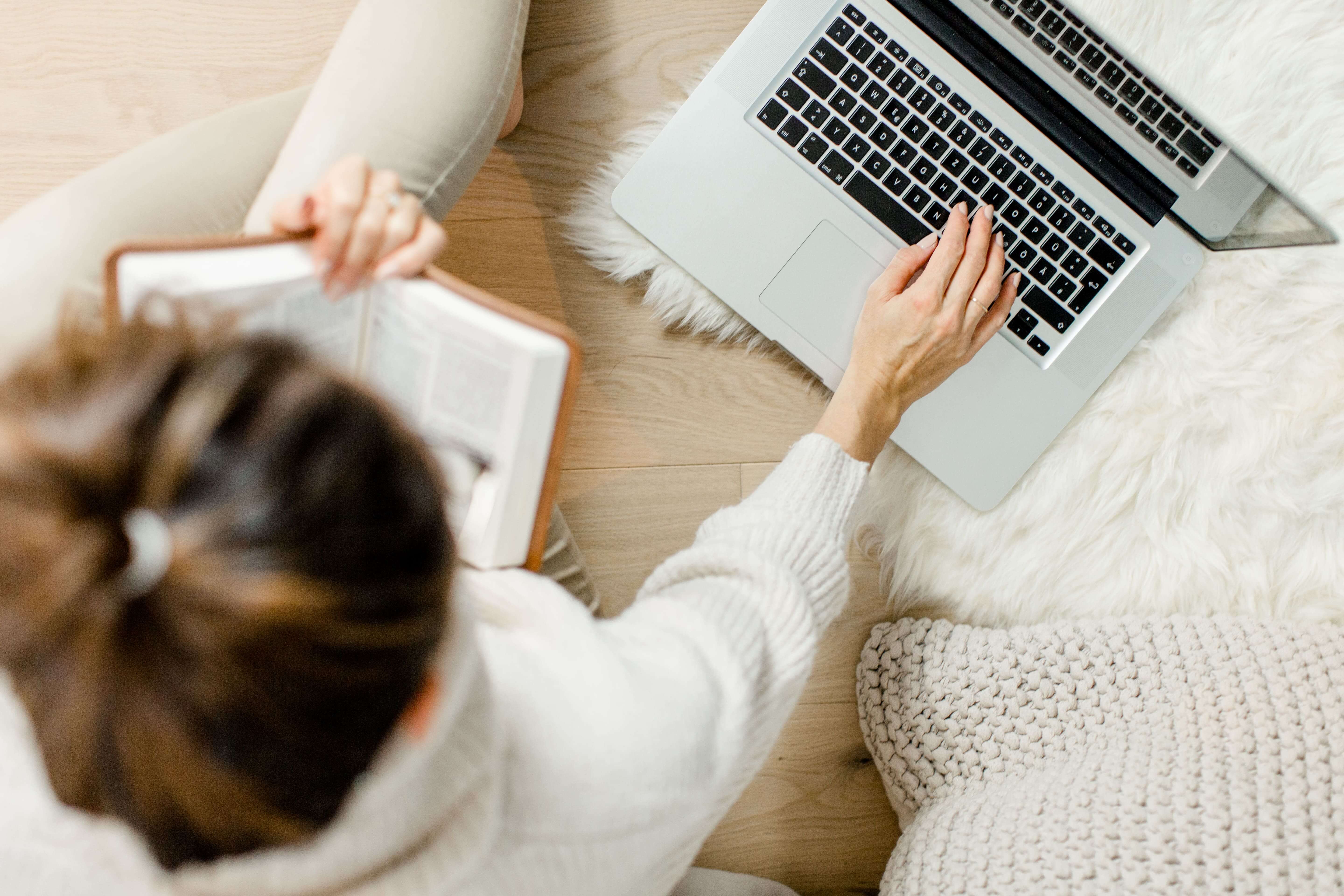 Frau mit braunem Dutt sitzt auf dem Boden mit Laptop und arbeitet. Sicht von oben
