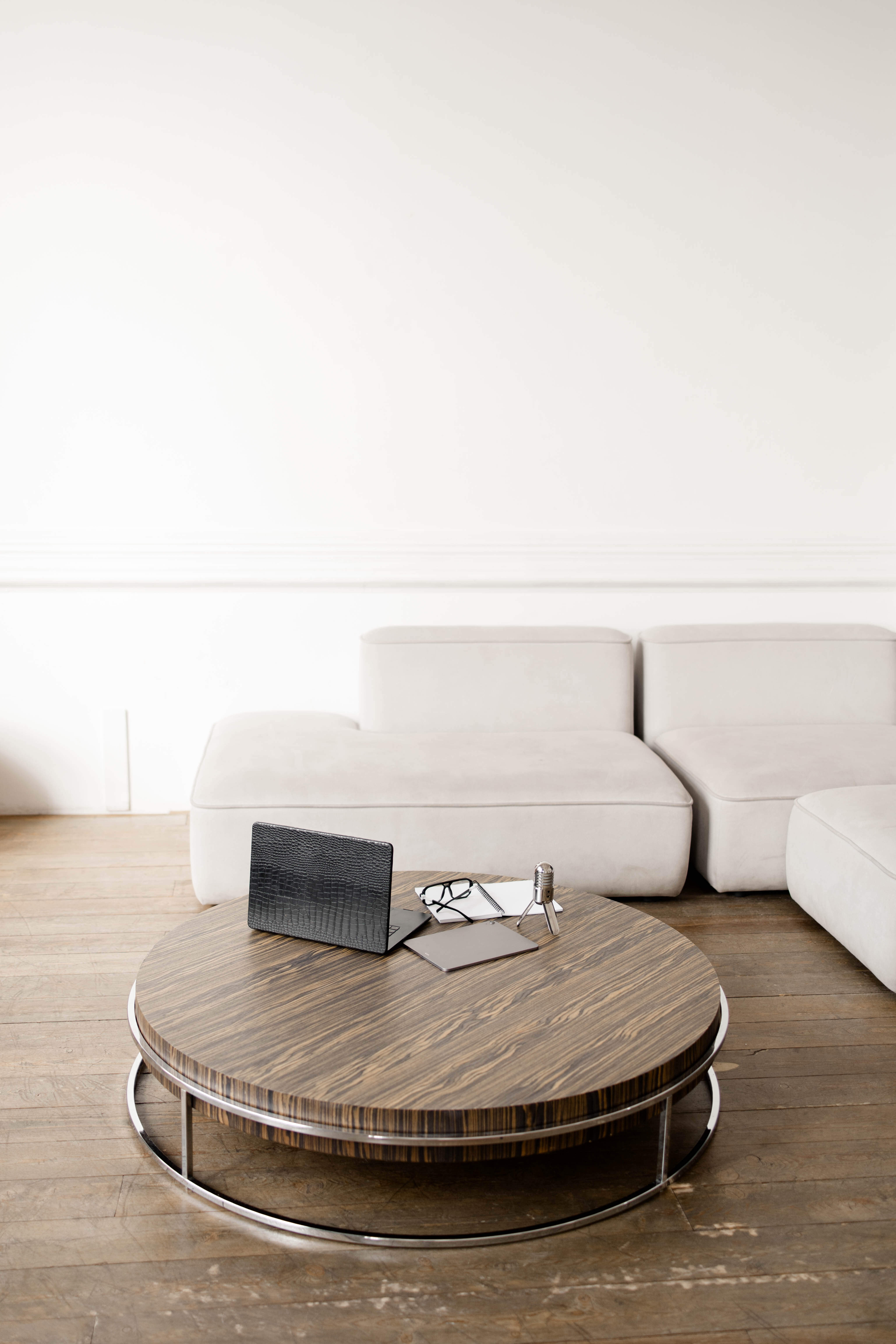 beige Sofaecke, runder Holztisch, darauf Laptop und ein paar Papiere