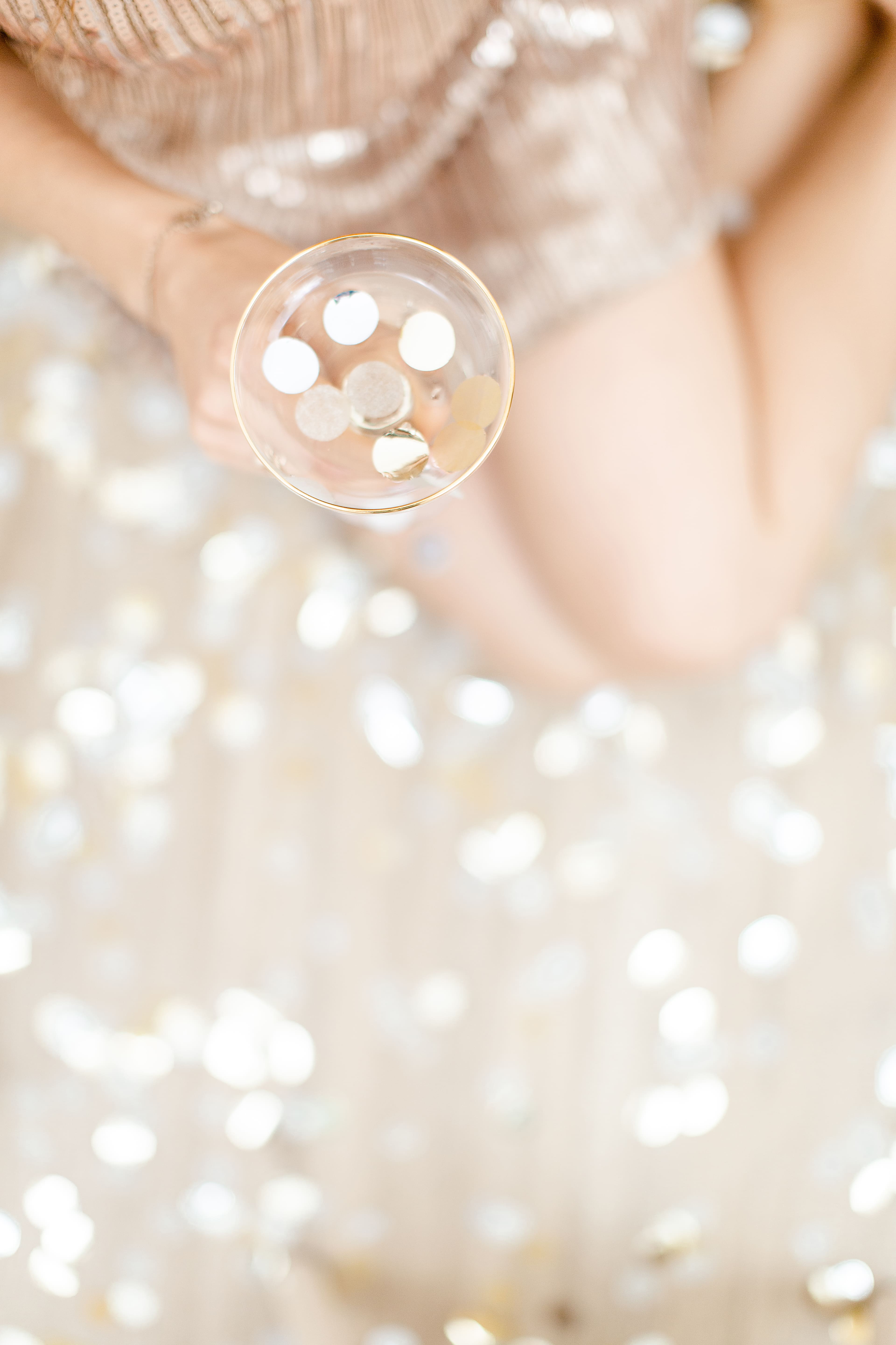 Frau, (ohne Gesicht) von oben fotografiert, mit Sektschale in der Hand, Glitzer rundherum, verschwommen