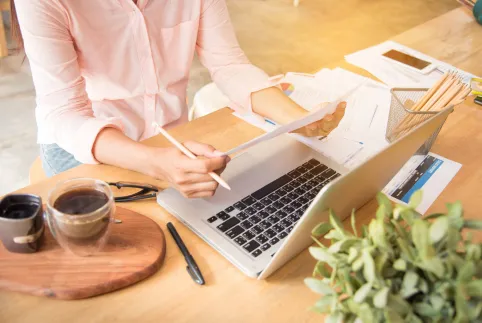 Woman at a desk with a laptop and papers and a coffee b her side
