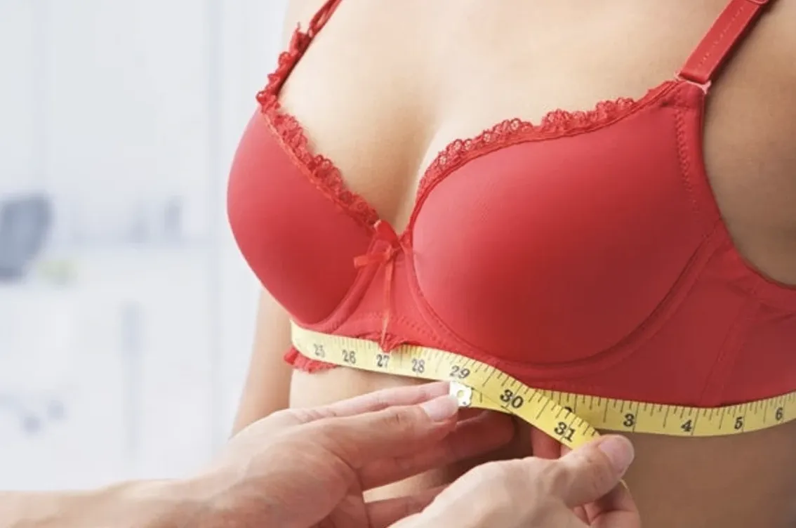 Woman in red bra with a professional bra fitter holding measuring tape
