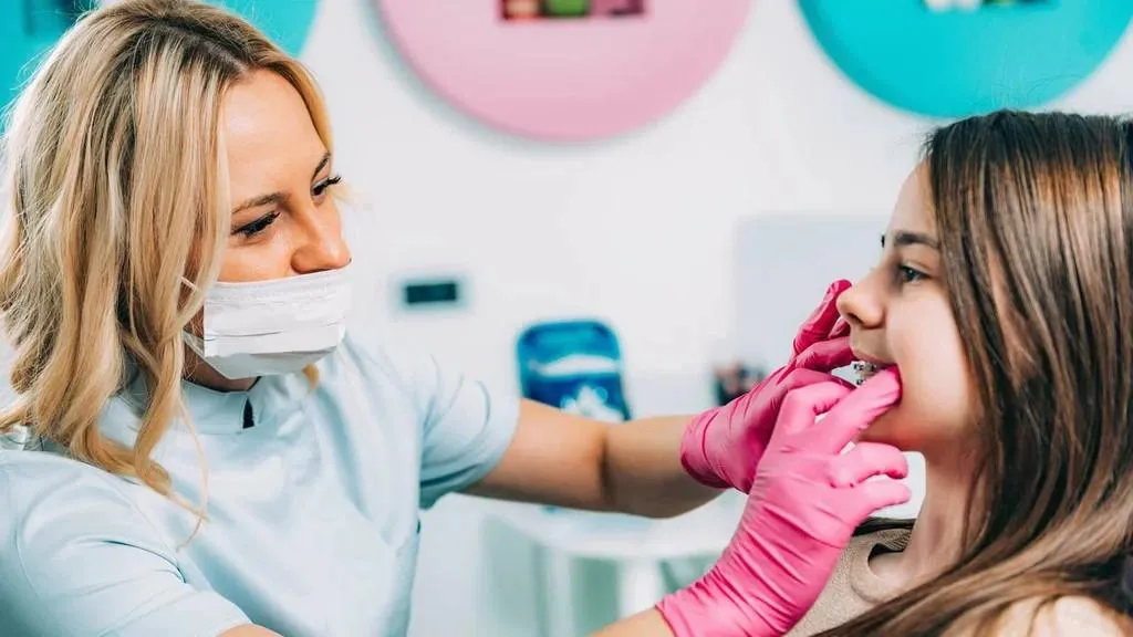 Dentist adjusting braces on a young woman in a colorful dental office.