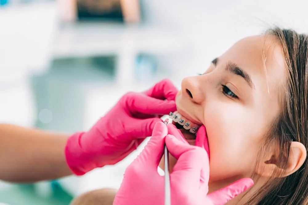 A young girl gets orthodontia treatment with braces from a dentist in pink gloves