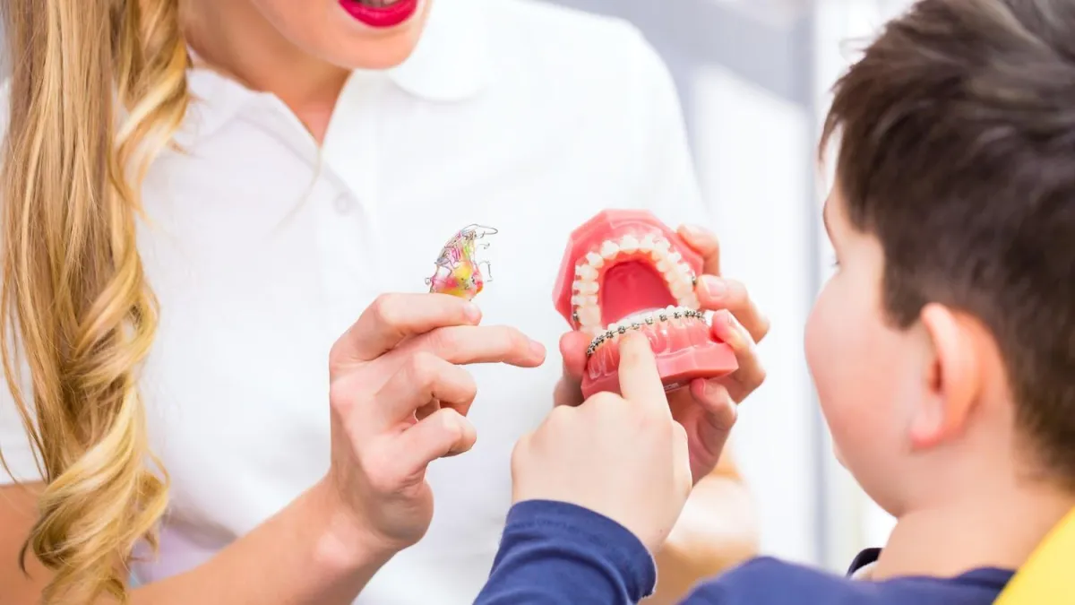 Dental professional showing a young boy a teeth model with braces in an educational setting