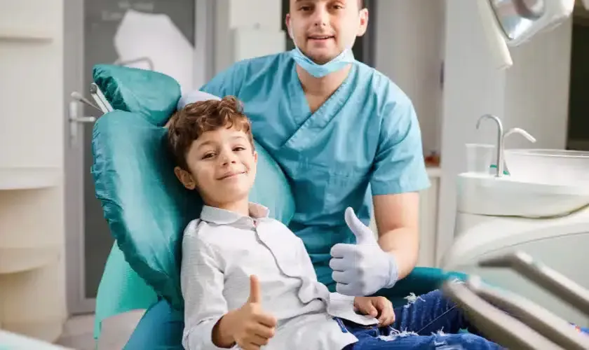 Smiling child in an orthodontic's chair and orthodontist giving thumbs-up