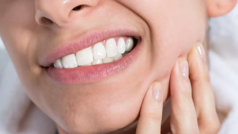 Close-up of a person clenching their teeth, holding their cheek in discomfort
