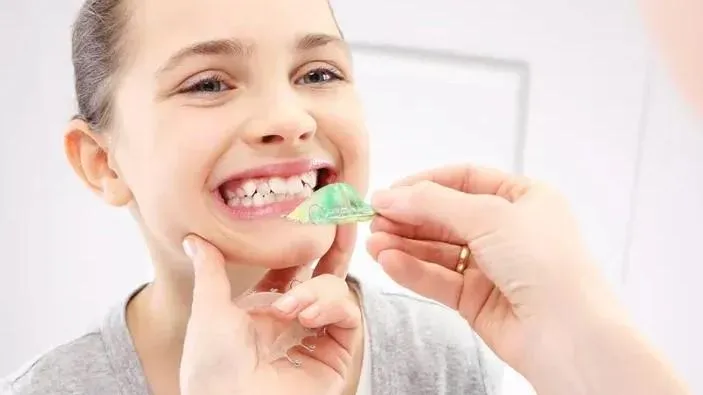 Smiling child with a green dental retainer being placed in their mouth.