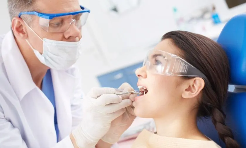 Orthodontist treats a young girl's tooth as she looks satisfied.