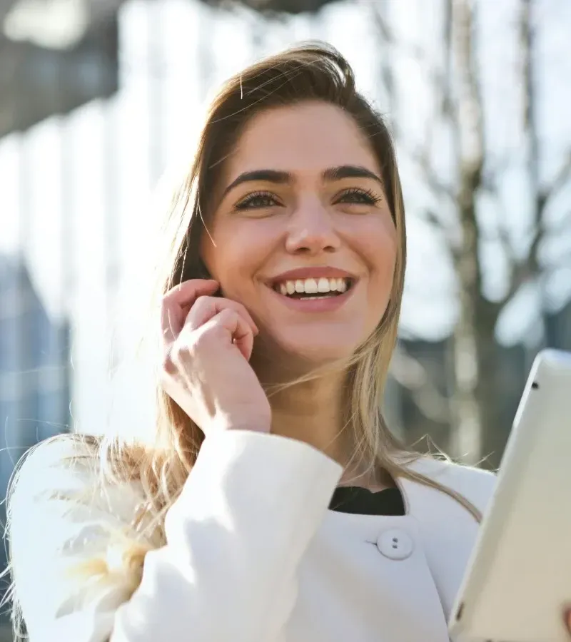 A female Ortho Admin Assistant with long hair smiling, on a smartphone, holding a tablet.