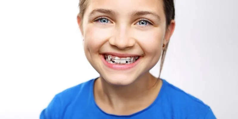 A young girl with blue eyes smiles, showing braces, wearing a blue shirt
