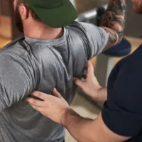 Personal trainer spotting someone do overhead free weight press