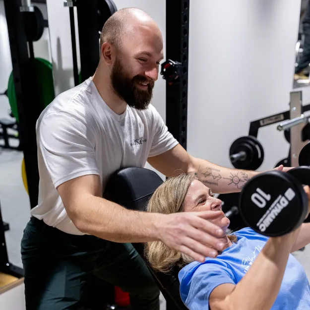 Personal trainer spotting someone do overhead free weight press