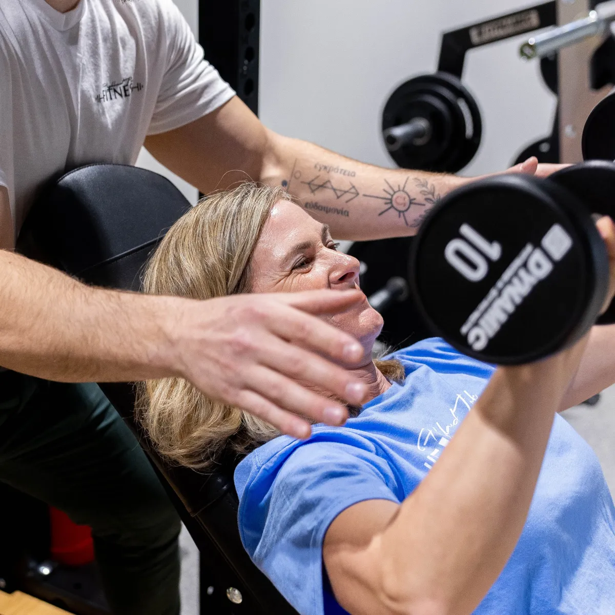Personal trainer spotting someone do overhead free weight press