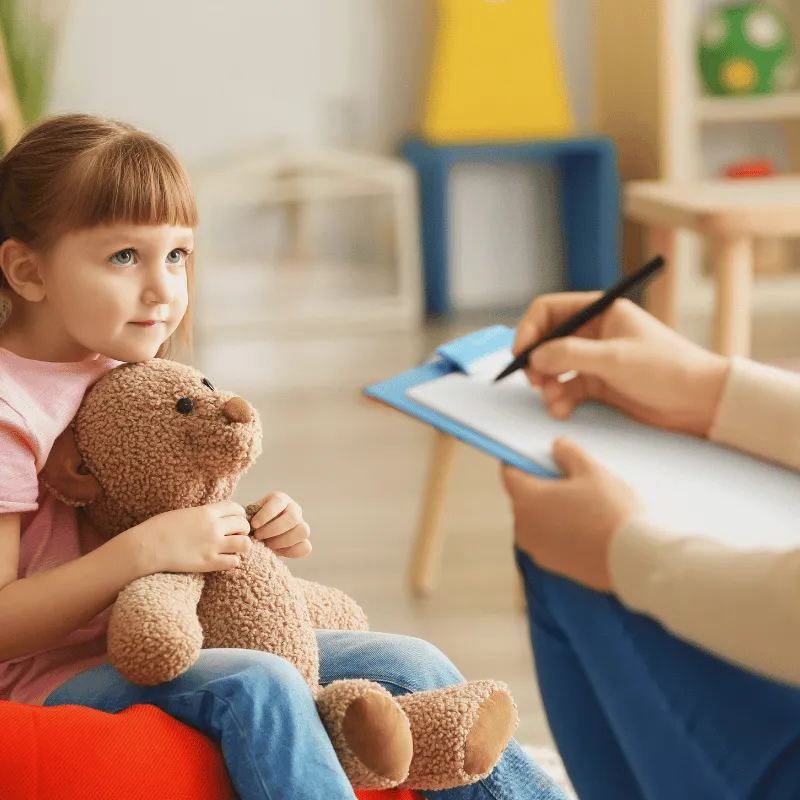 A young girl holding a teddy bear in a CBT therapy session