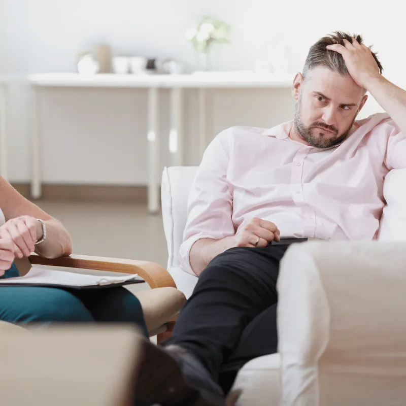 A man brushing his hair as he looks down at therapist clipboard