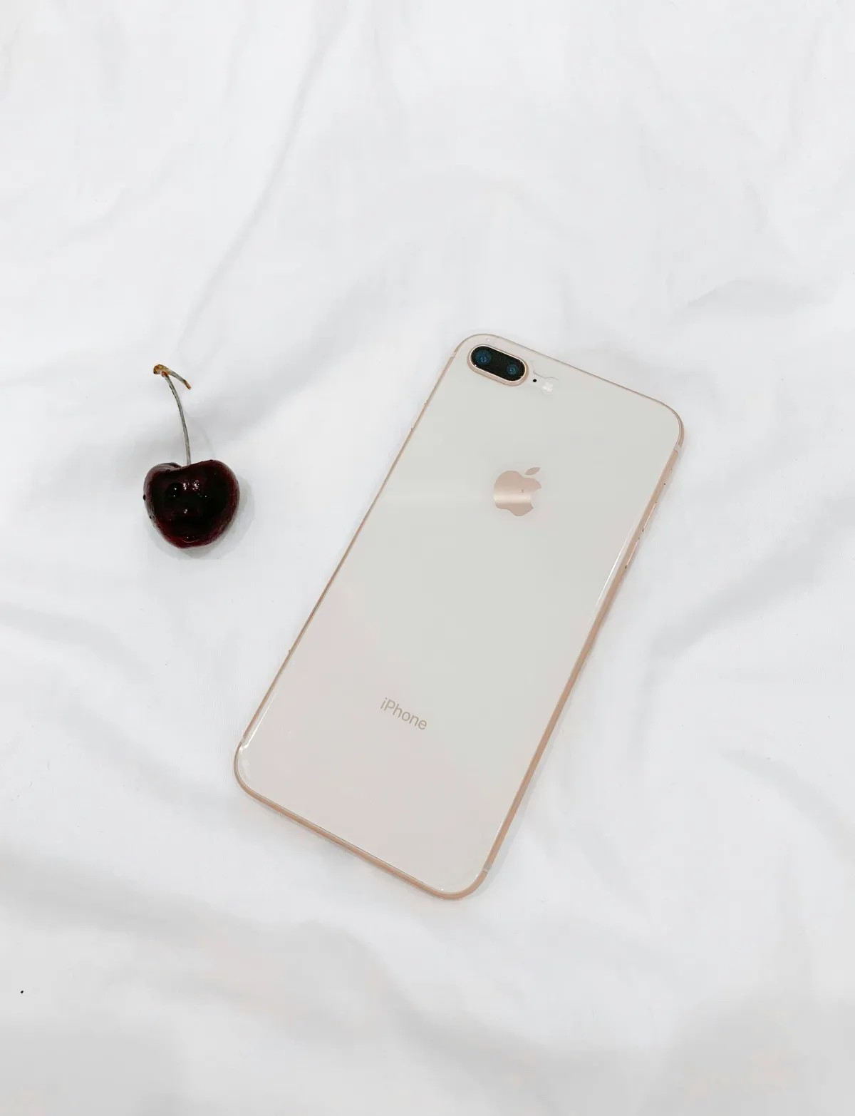A cherry and an iPhone laying facedown on white fabric
