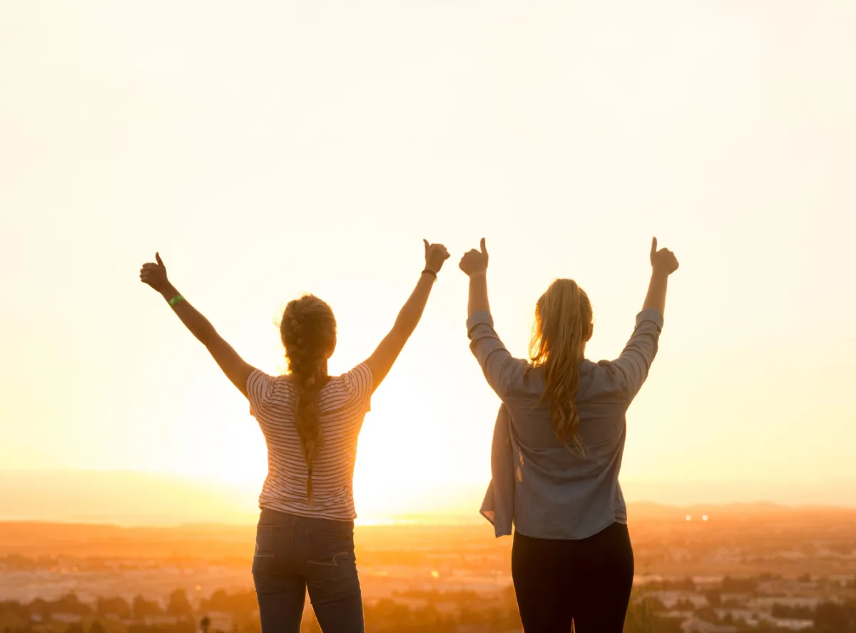 two females looking out to the sunset giving the thumb up