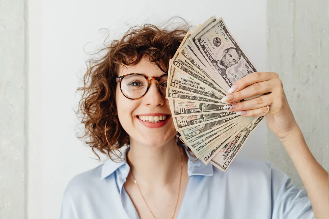 Smiling business owner holding a fan of cash, representing profit kept through proactive tax strategy