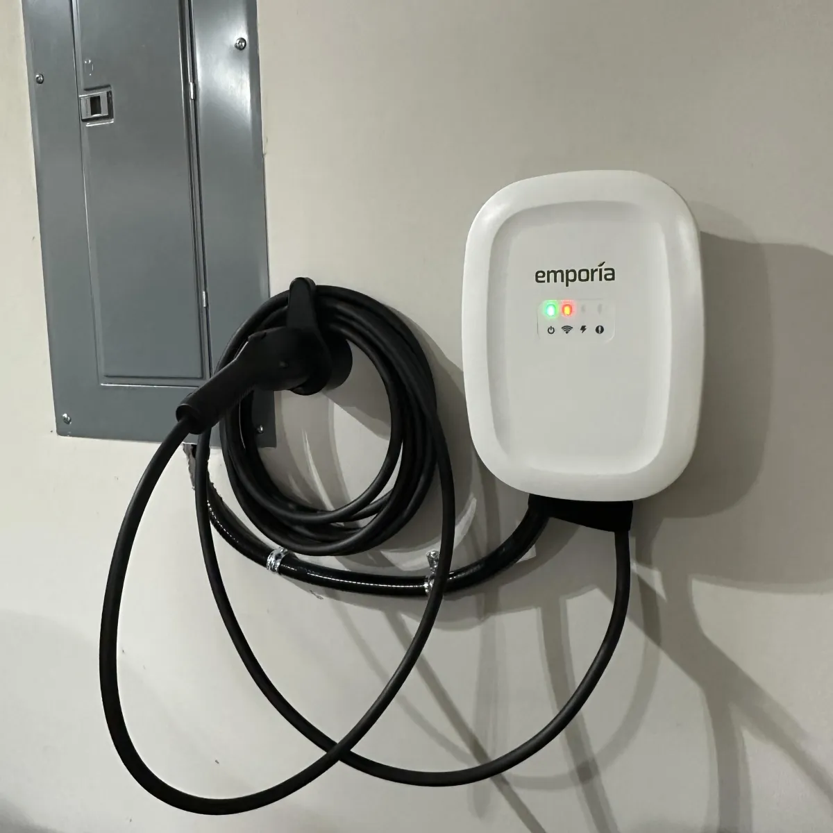 EV charger installation on wall with charging cable, featuring Emporia branding and indicator lights, emphasizing home electric vehicle charging solutions.