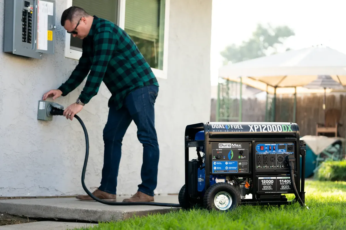 Man connecting a generator inlet to a home electrical panel, with a DuroMax dual fuel generator nearby, illustrating safe power backup solutions for outages.