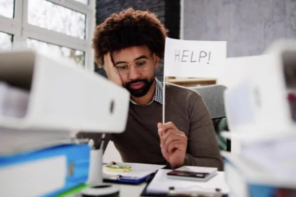 Image of man behind notebooks holding help sign