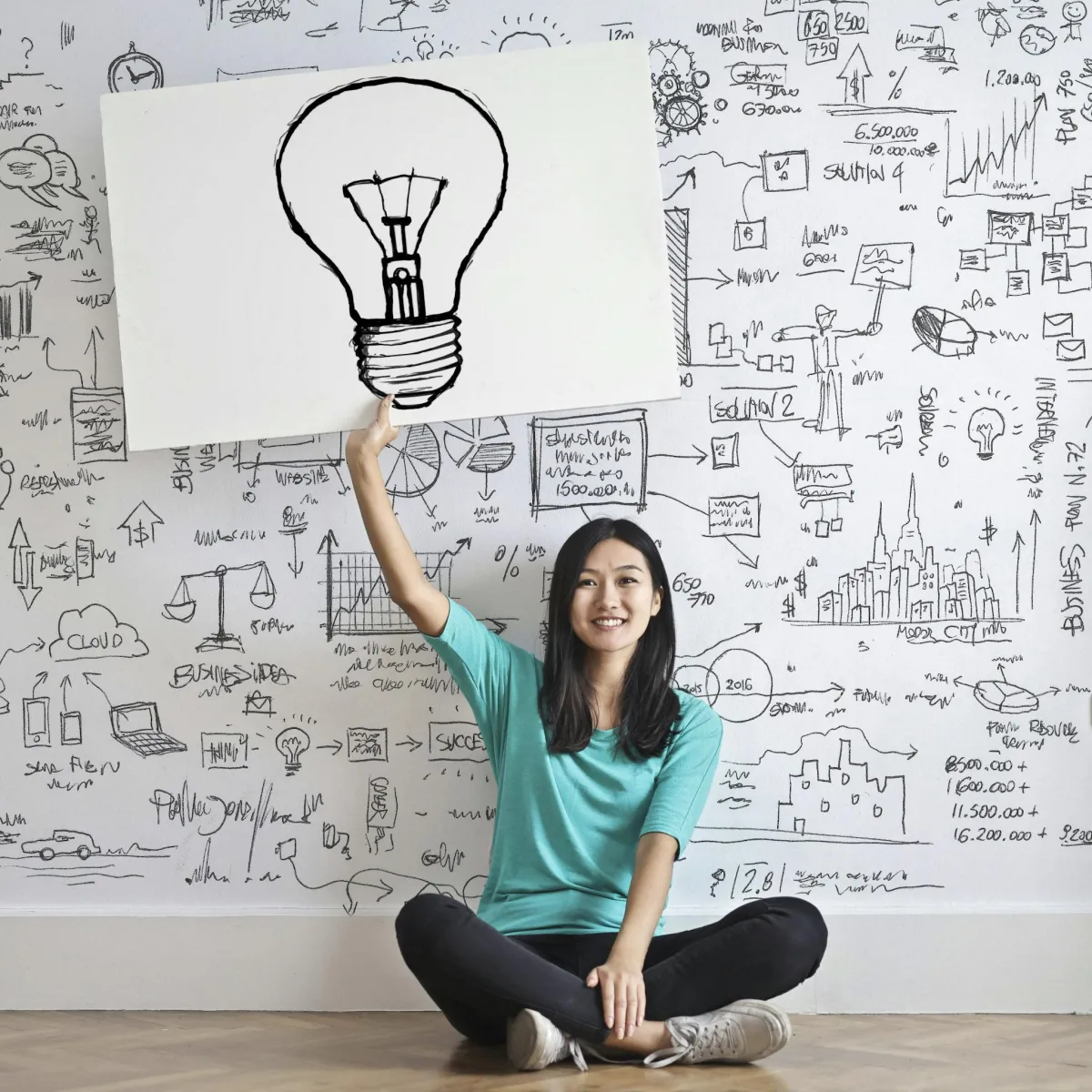 image of woman sitting on floor holding a poster board with a lightbulb drawing